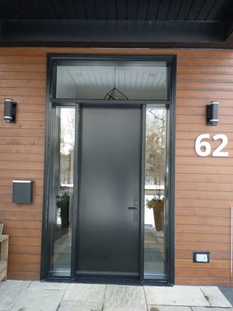 Black modern entry door with a sidelight and transom on wood siding