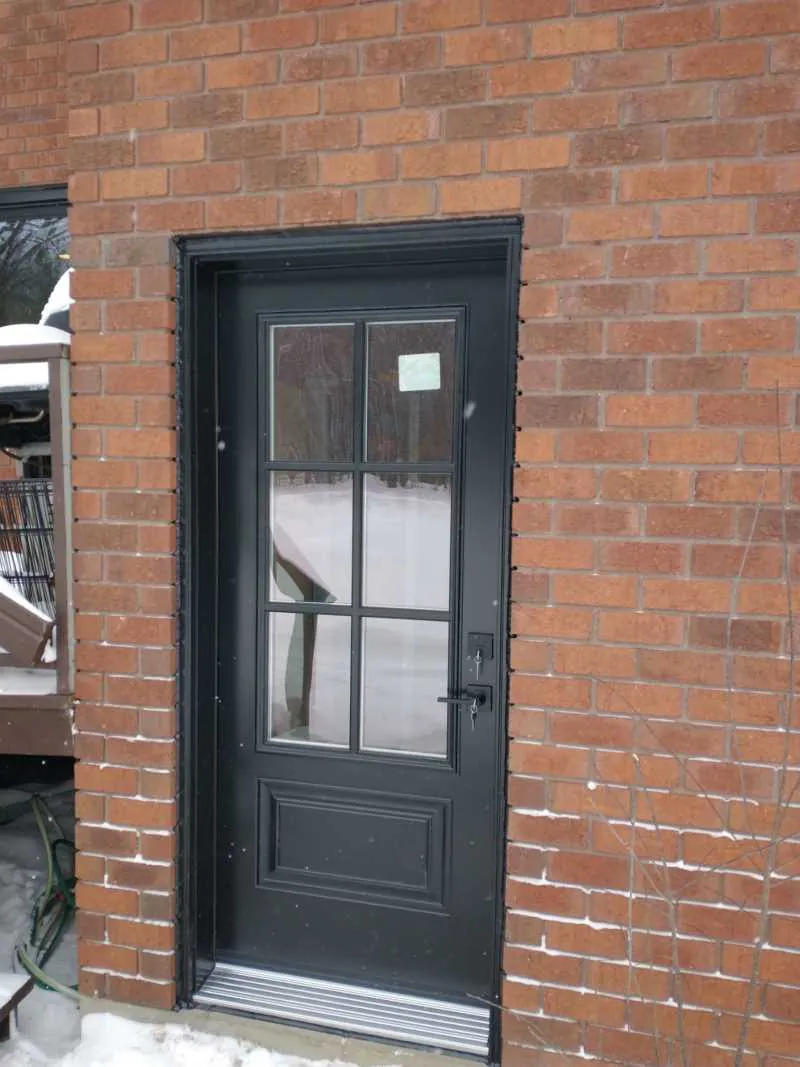 Black entry door with grilled glass on red brick