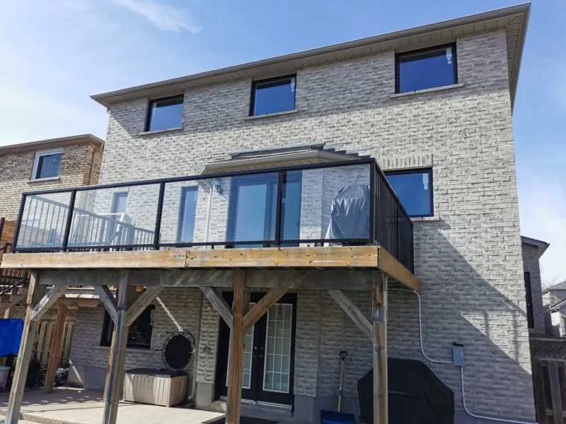 New black windows on a grey brick home with a glass balcony