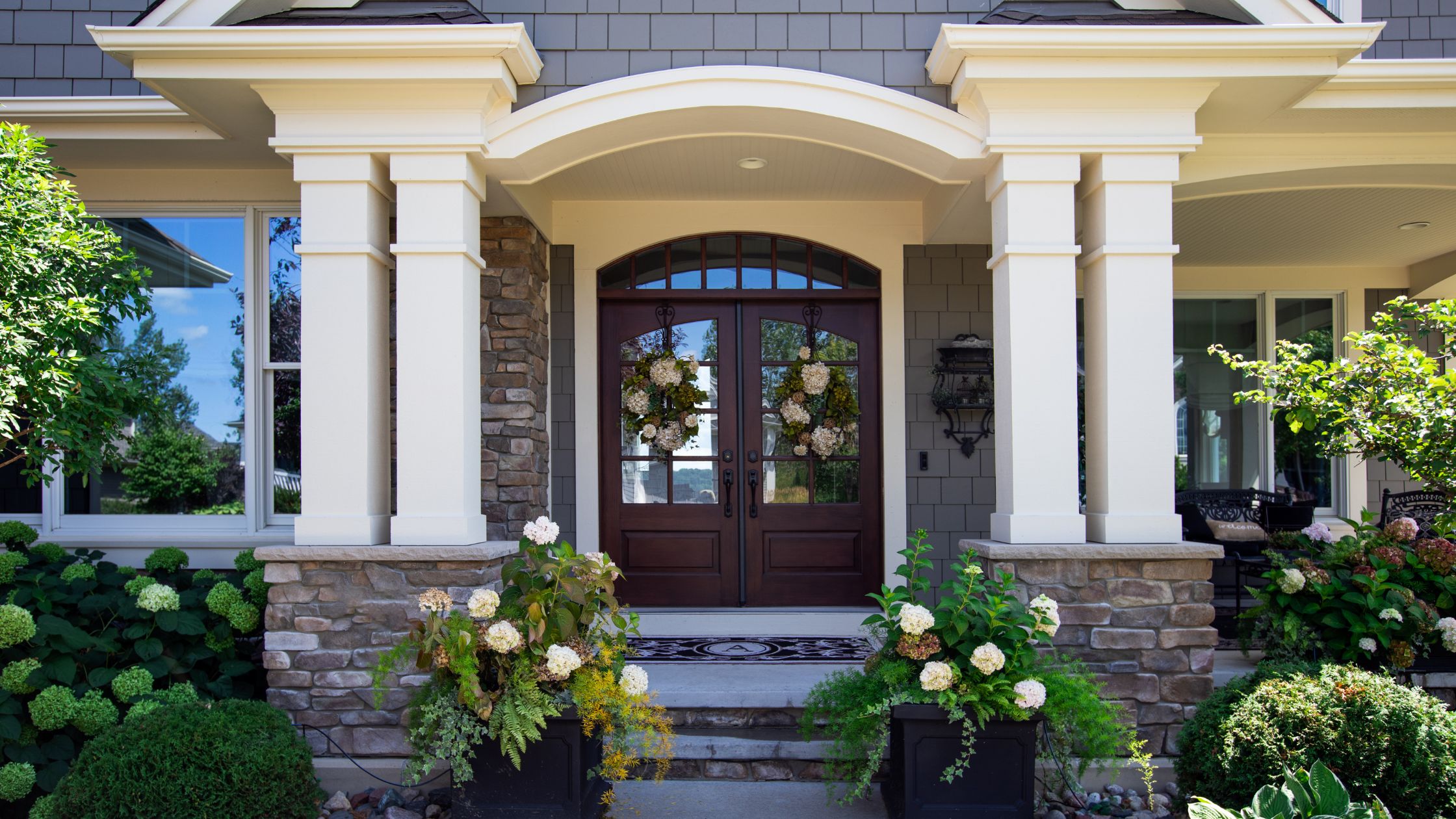 Front entrance featuring modern double wooden doors with glass inserts and floral wreaths, showcasing the benefits of replacing old wooden doors.