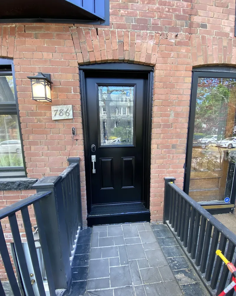 Storm Door Swapped for a Black Steel Door: after Front door on a brick porch with railings after replacement
