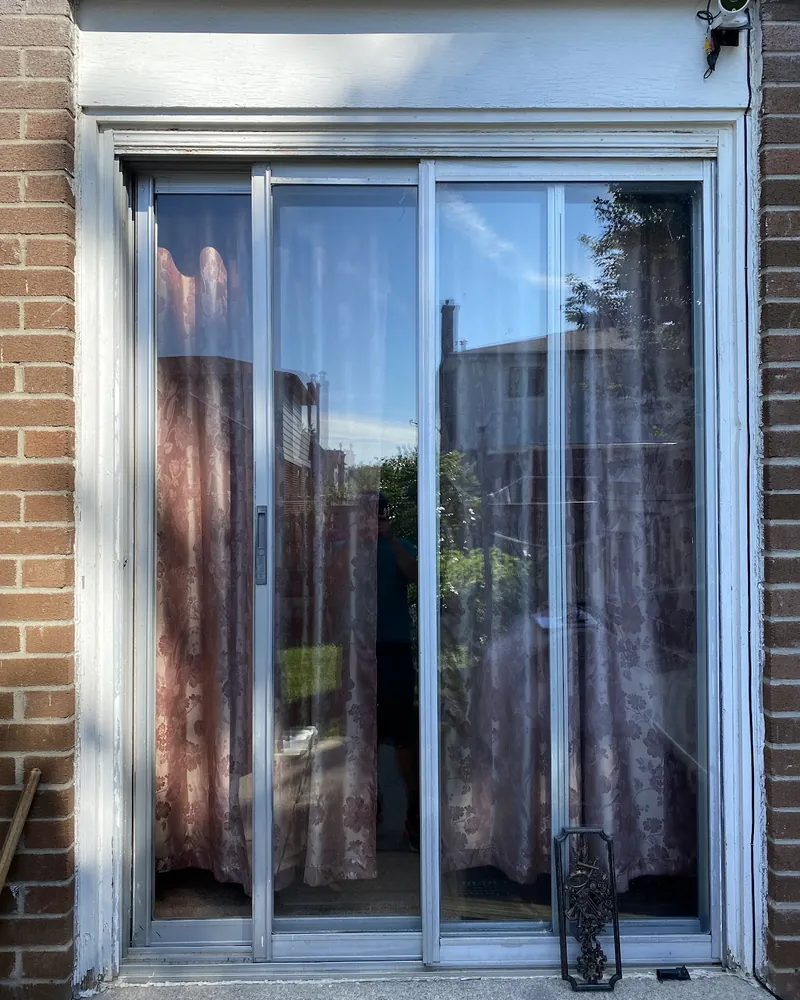 Aluminium Patio Door to New Vinyl Slider: before Sliding patio door on a brick wall before replacement in Brampton