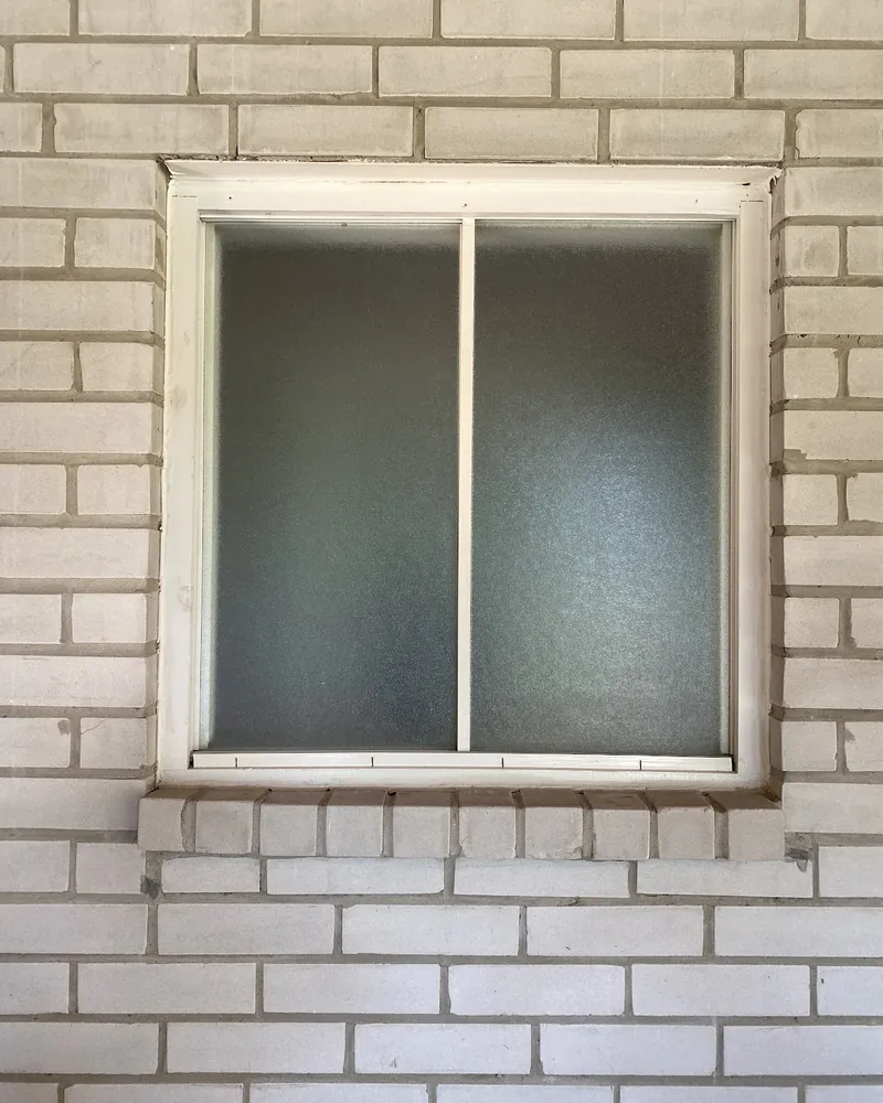 Frosted Slider to New Window: before Window on a painted brick wall before replacement